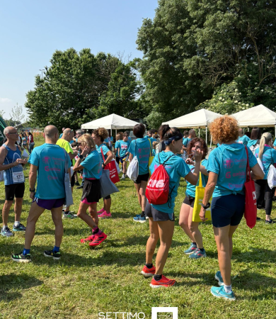 Partecipanti all’evento sportivo outdoor organizzato da Gelsia, riuniti in un’area verde sotto gazebo bianchi in una giornata di sole. I partecipanti indossano magliette personalizzate con il logo Gelsia, zainetti colorati e abbigliamento tecnico sportivo. Evento aziendale dedicato allo sport, al benessere e alla socializzazione.